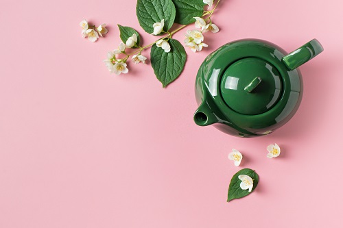 green tea pot with leaves on pink background